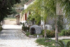 A stone pathway leading to a white building with a stone archway and a small garden with various plants and flowers. - Casa Laura di fronte la Tonnara (San Vito Lo Capo)
