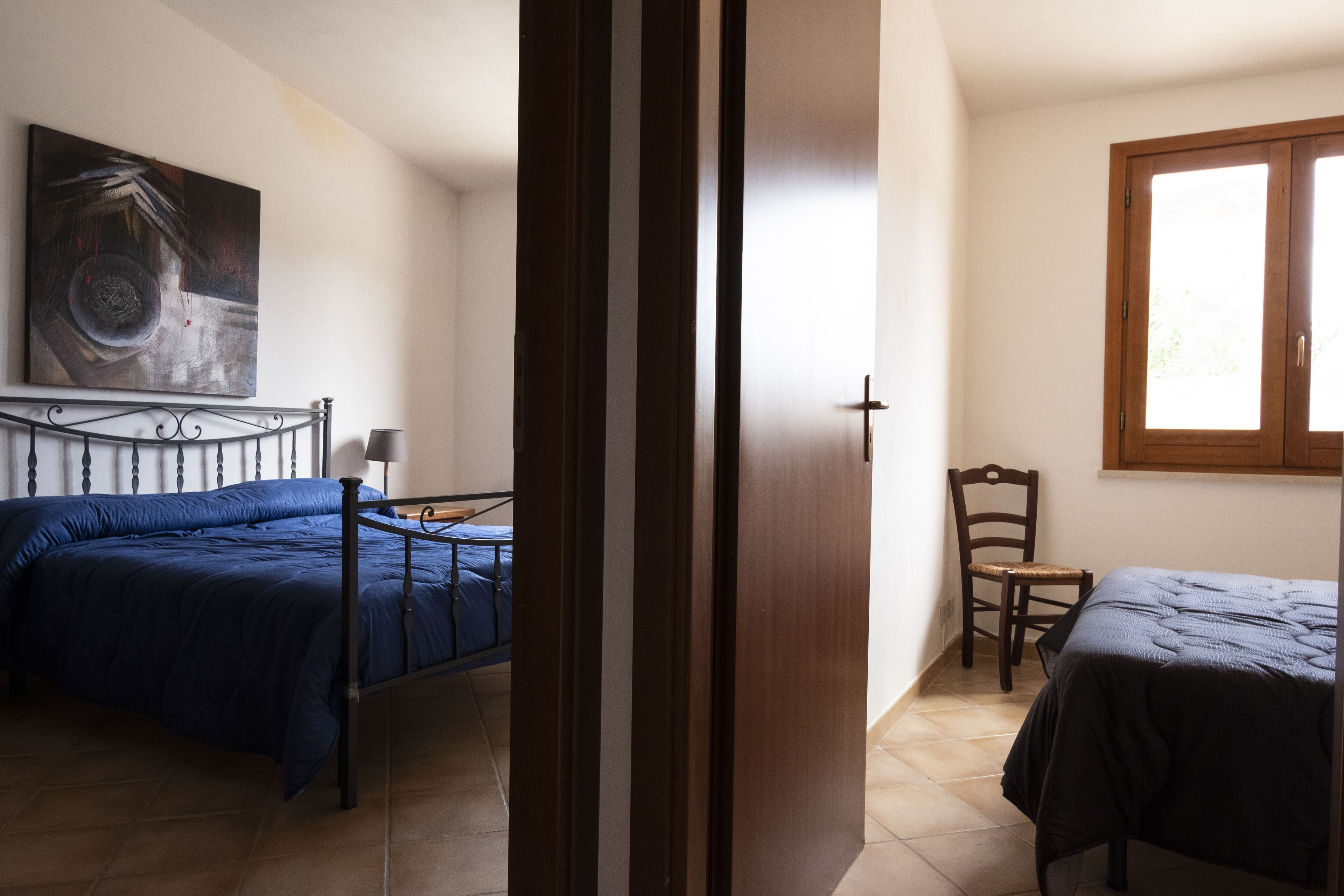 Un dormitorio con dos camas, una puerta de madera, una silla y un cuadro en la pared.