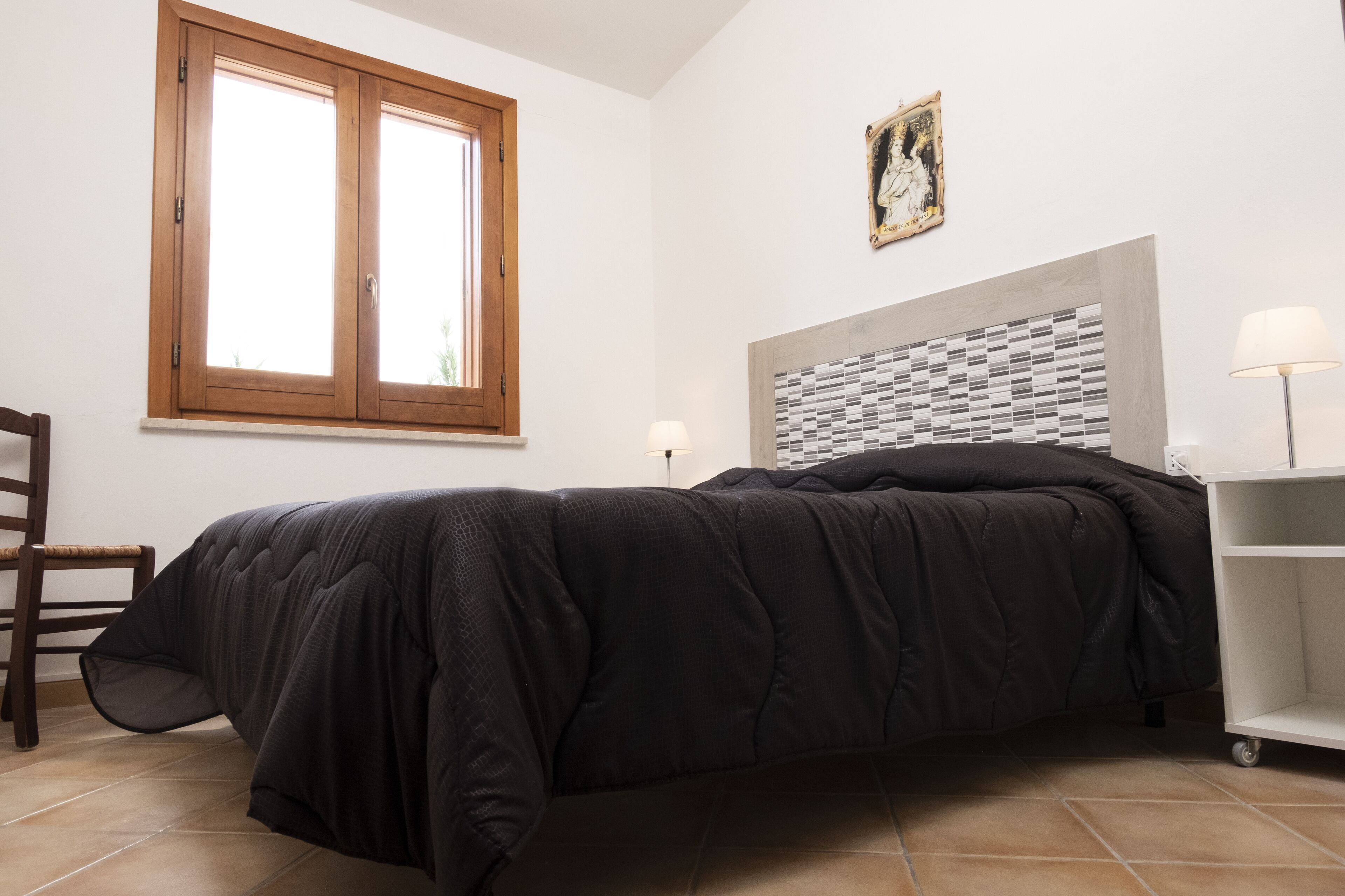 A bedroom with a bed, a window, a chair, a lamp, and a painting on the wall.