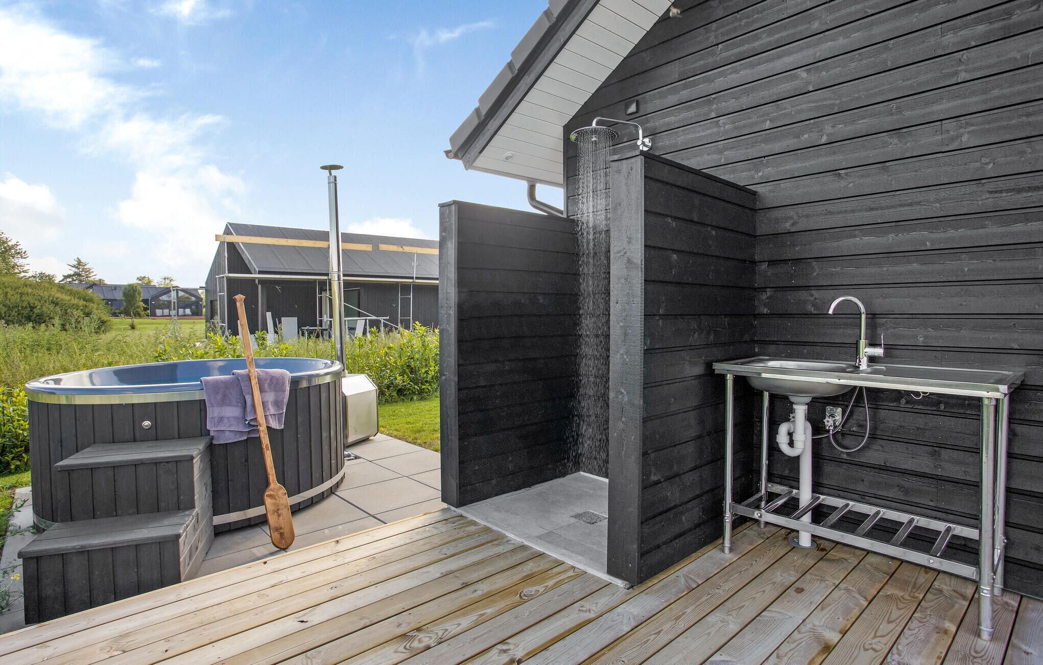 A hot tub, a wooden deck, and a sink with a showerhead.