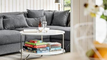 A modern living room with a grey sofa, a round coffee table with a stack of board games, and a lamp.