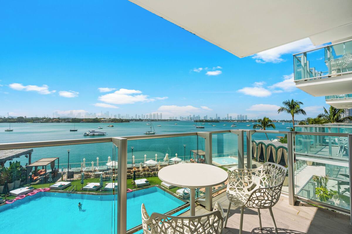 A balcony with a pool, lounge chairs, and a table overlooking a marina with boats.