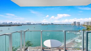 A balcony with a glass railing overlooking a marina with boats and a city skyline.