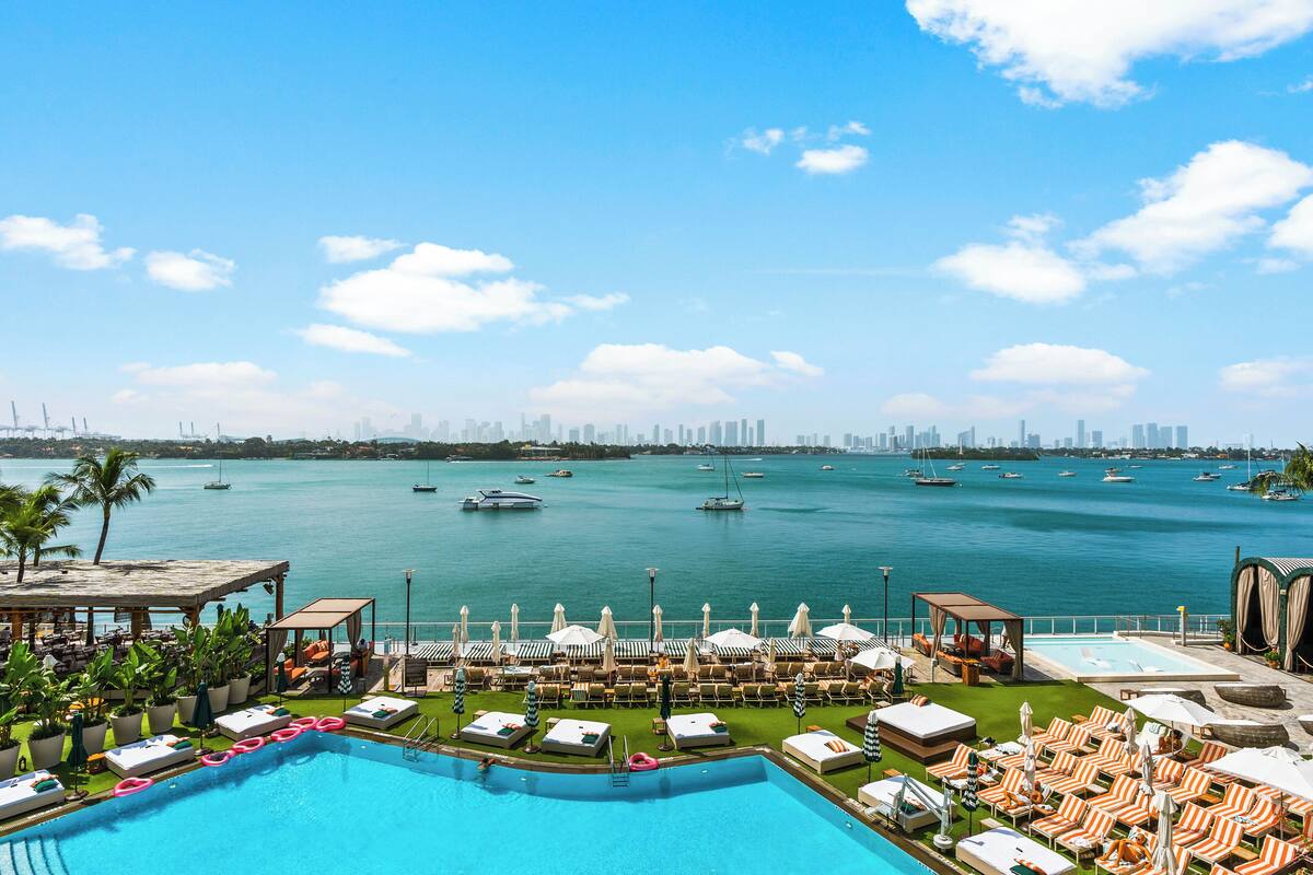 A poolside area with lounge chairs and umbrellas, a clear view of the water, and a city skyline in the distance.