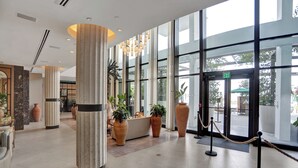A spacious lobby with large columns, potted plants, and a glass entrance.
