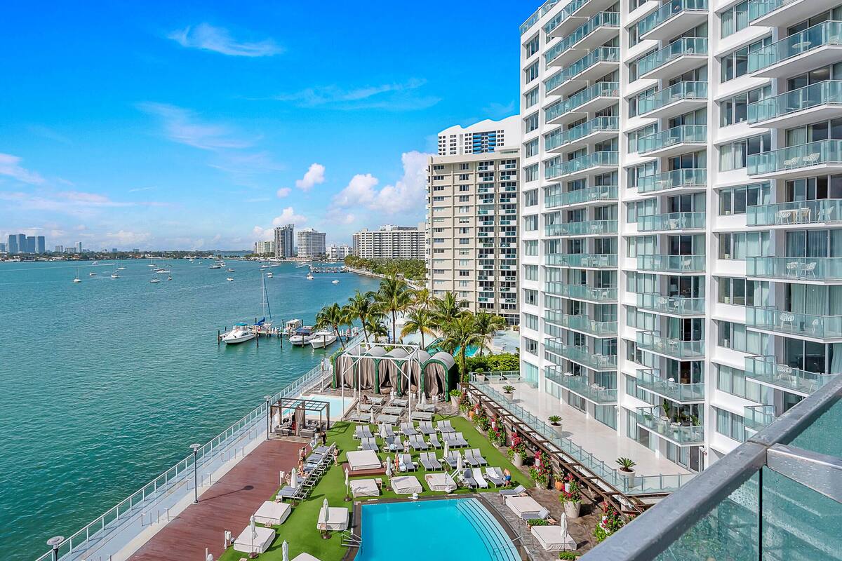 A high-rise hotel with a rooftop pool overlooking a marina with boats.