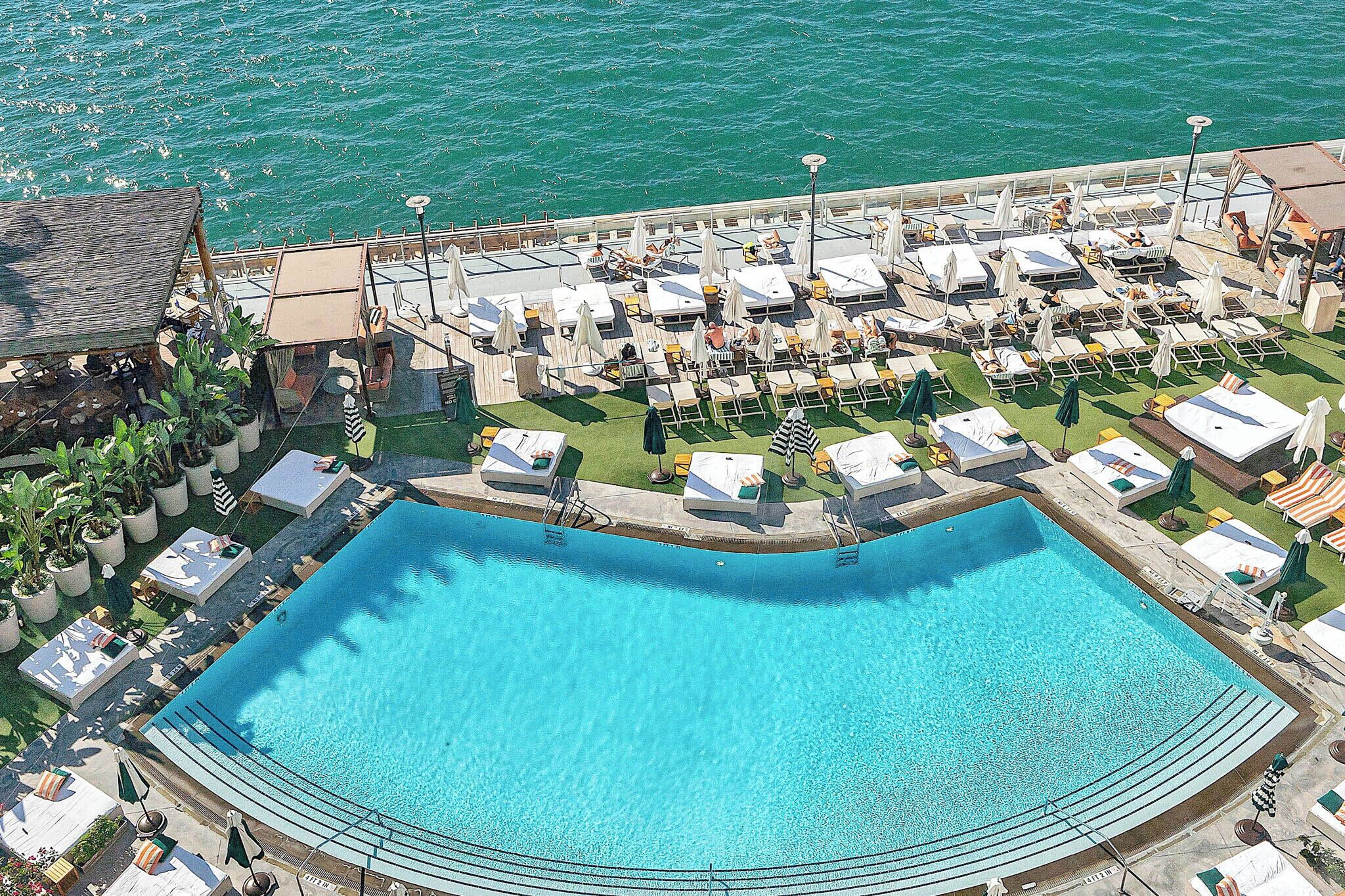 An aerial view of a resort with a large pool, sun loungers, and umbrellas.