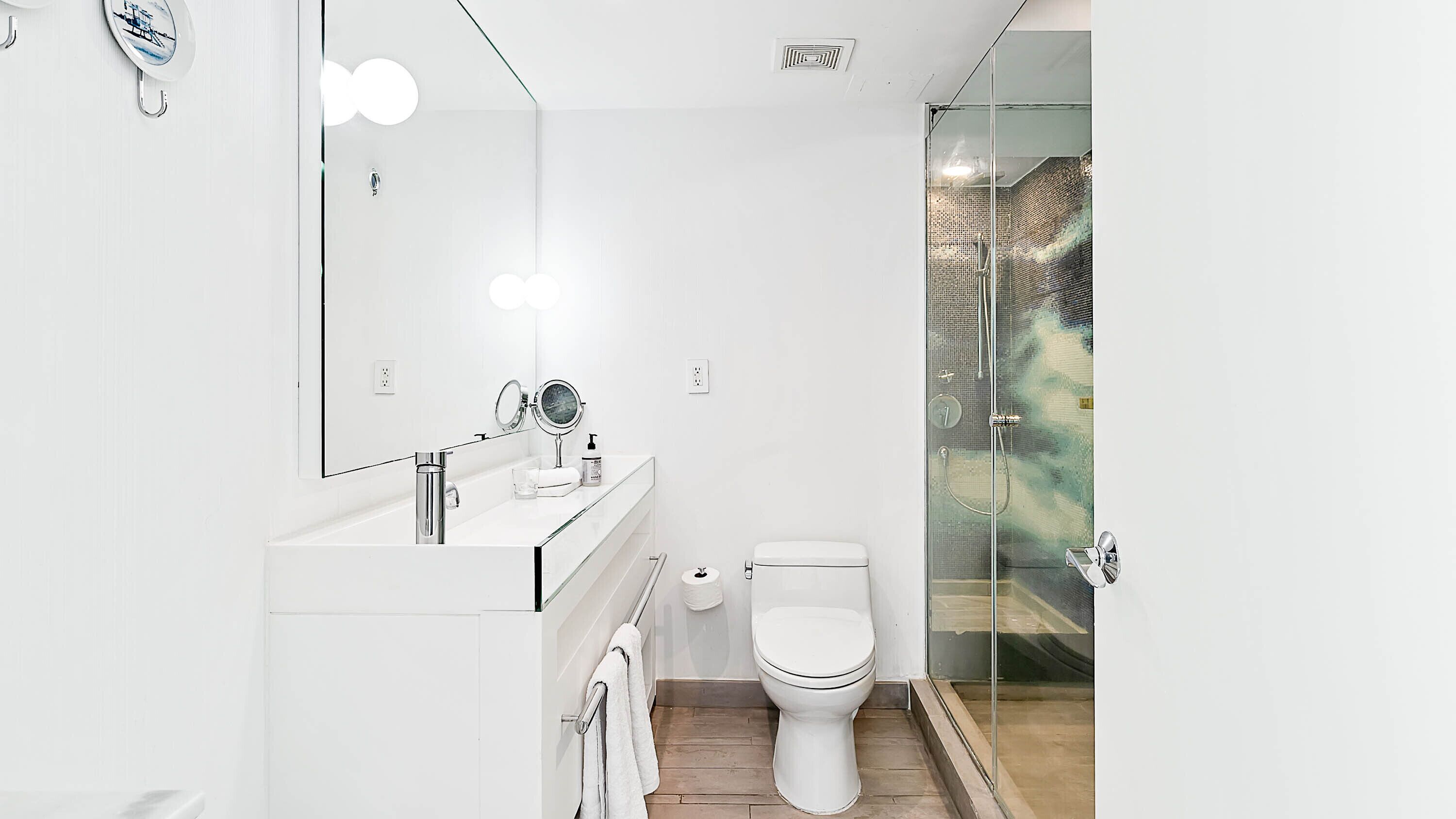 Un baño moderno con cabina de ducha de vidrio, inodoro blanco y tocador con espejo e iluminación.
