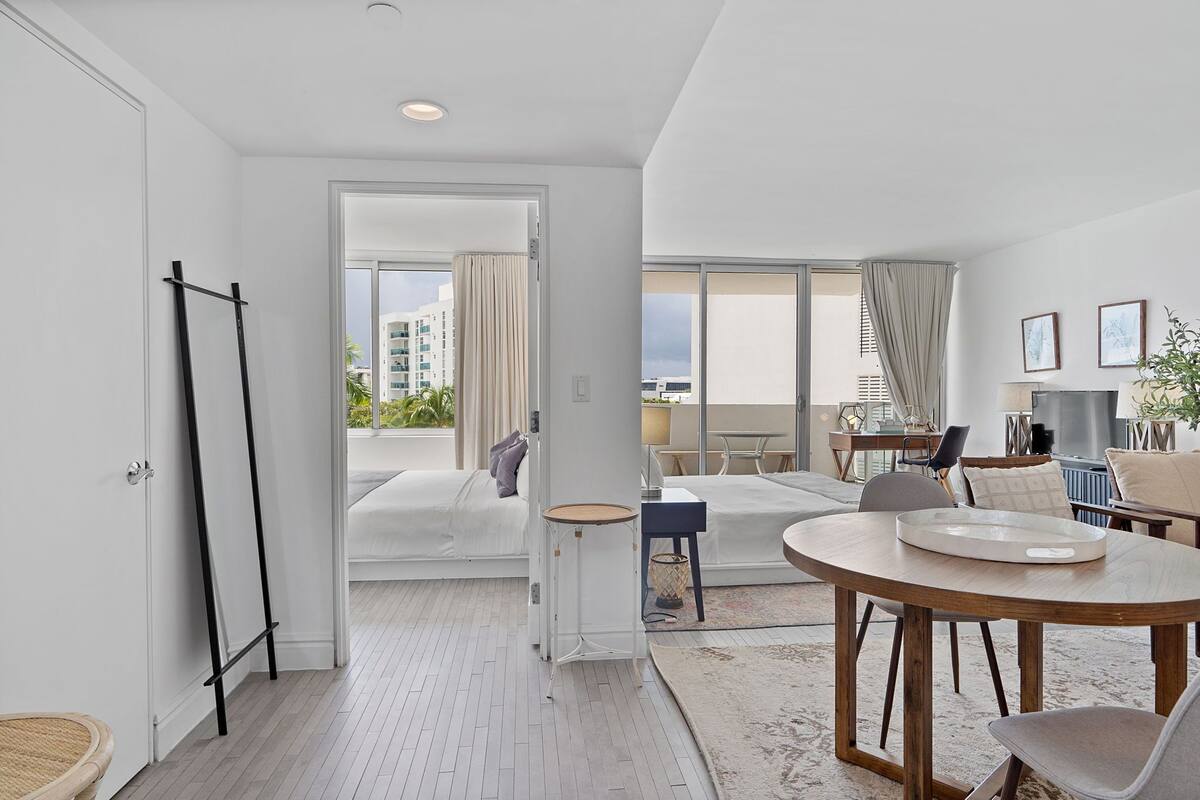 A modern hotel room with a balcony, a dining area, and a view of the cityscape.