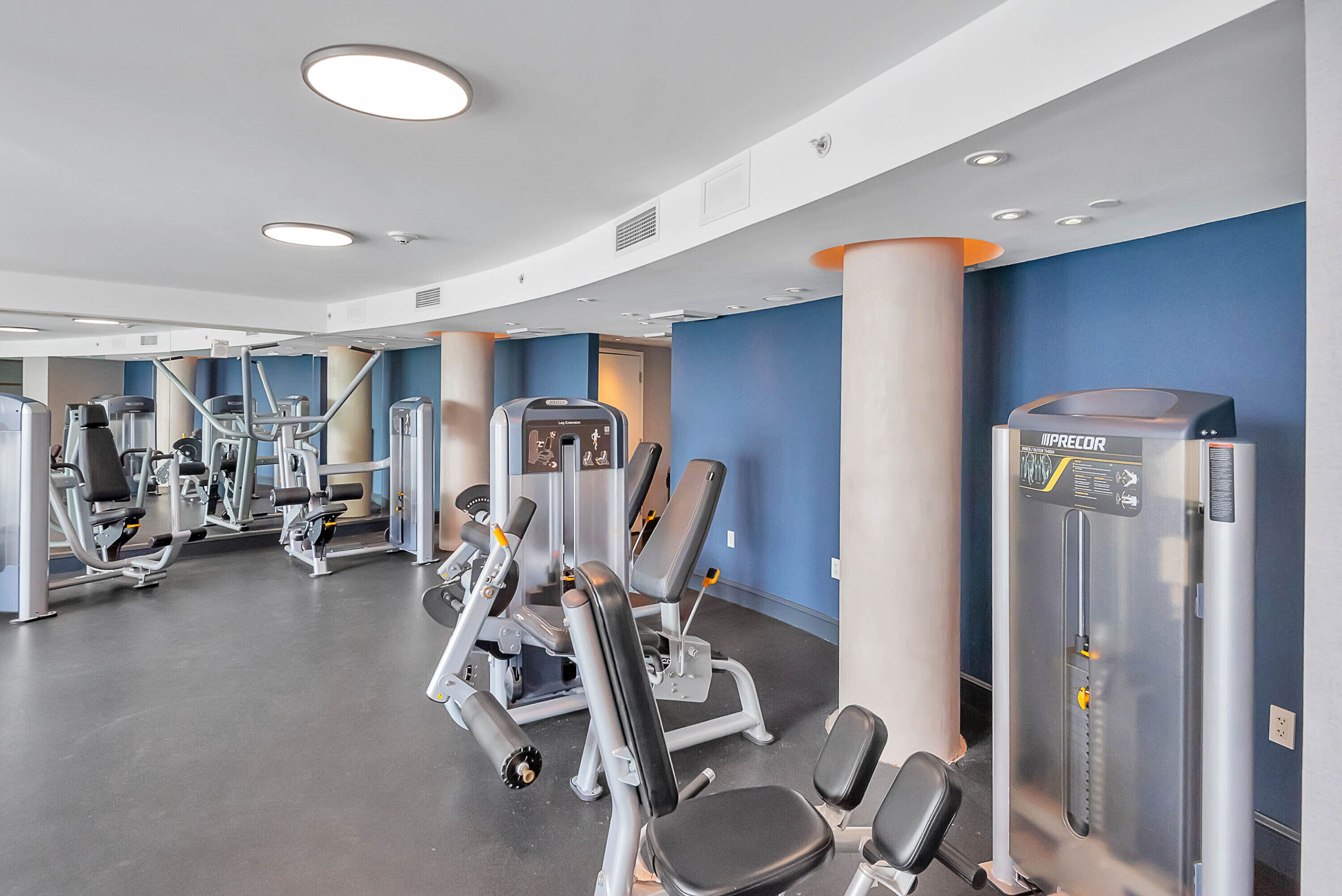 Un gimnasio con diversas máquinas de ejercicio, un espejo grande y un dispensador de agua en la pared.