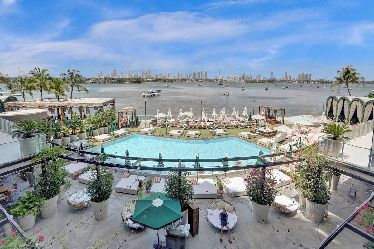 A rooftop pool area with lounge chairs, umbrellas, and potted plants.