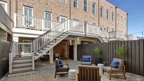 A brick building with a staircase leading to a balcony. There are outdoor seating areas with chairs and a table.