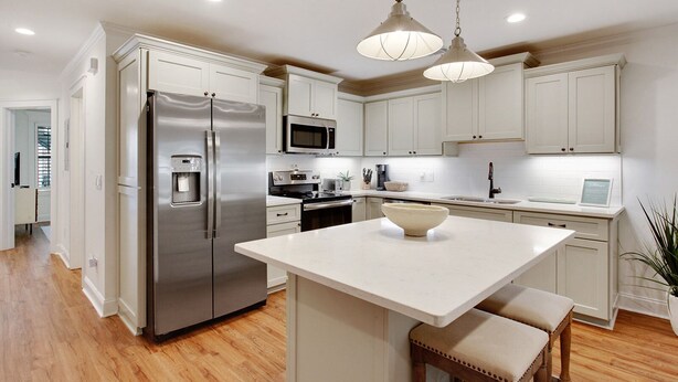 A modern kitchen with white cabinetry, stainless steel appliances, and a central island with seating.
