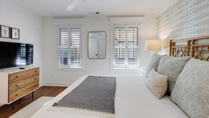 A bedroom with a bed, a TV, a dresser, and a ceiling fan.