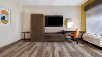 Una habitación de hotel moderna con una cama grande, un escritorio con silla, un televisor de pantalla plana, un espejo y un radiador.