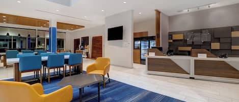 Un hall de hotel con mostrador de recepción, zona de estar con sillas y una máquina de café.