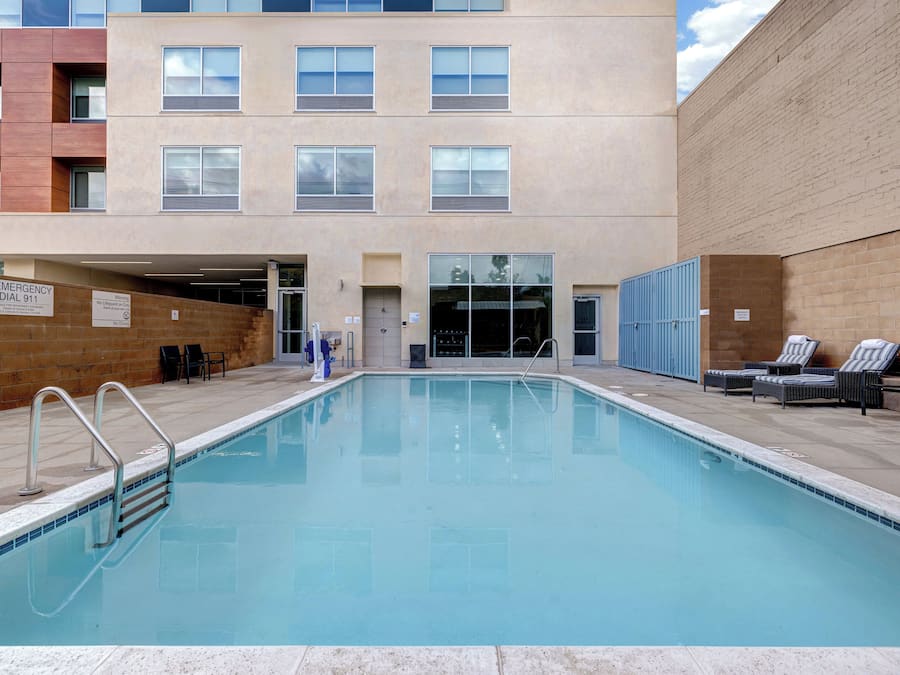 A swimming pool with a lifeguard stand, lounge chairs, and a building with multiple windows in the background.