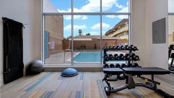 Academia com equipamentos de ginástica, piscina e vista para um edifício.