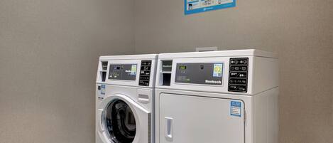 Un área de lavandería con dos máquinas blancas, cada una con pantalla digital y un letrero de PayRange.