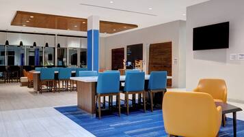 A modern dining area with blue and yellow chairs, a coffee machine, and a flat-screen TV on the wall.