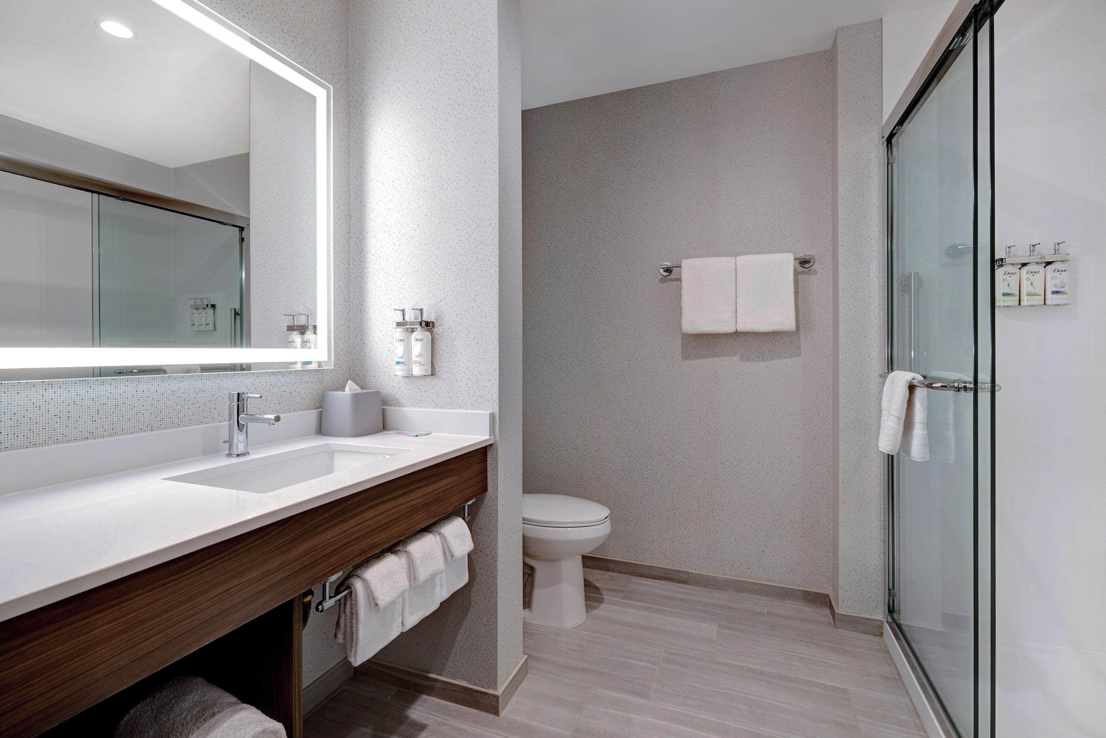 Un baño moderno con un espejo grande, un lavamanos, un inodoro y una cabina de ducha de vidrio.