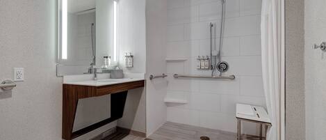 Un baño moderno con ducha, tocador con espejo y una pequeña mesa.