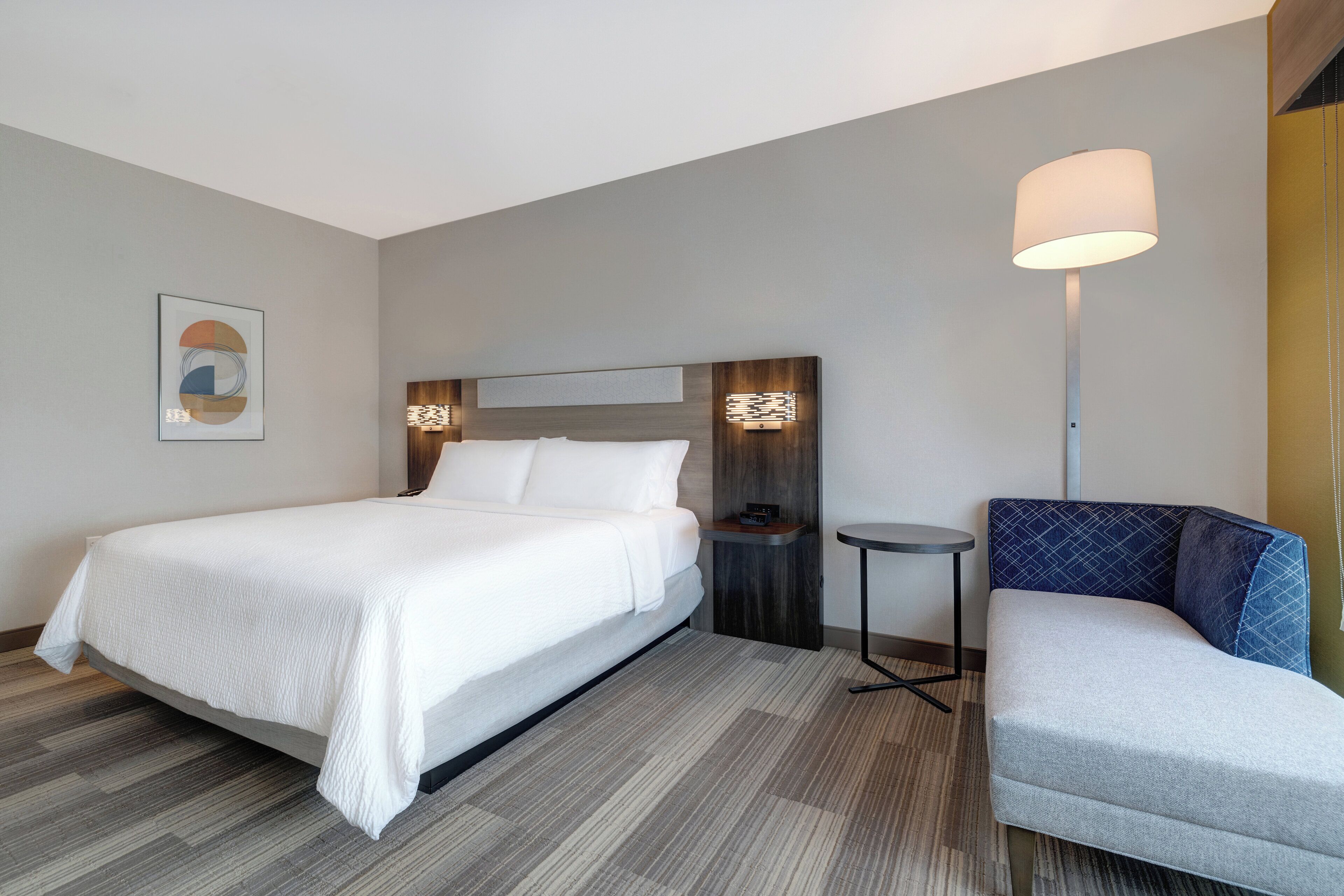 A hotel room with a bed, bedside table, lamp, and a seating area.