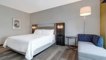 A hotel room with a bed, bedside table, lamp, and a seating area.