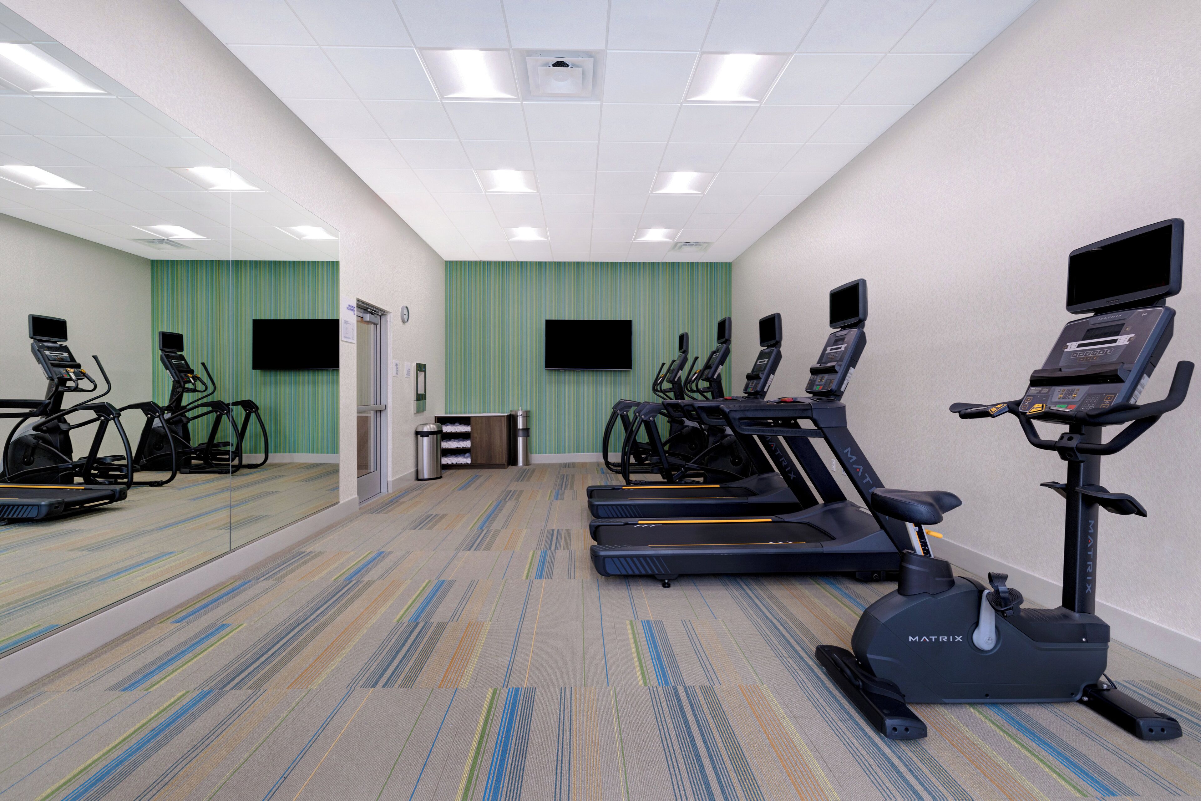 Un gimnasio con cintas de correr, bicicletas estáticas y un espejo grande.