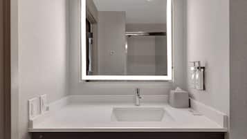 Un baño con lavamanos blanco, un espejo con luz y un dispensador de toallas.