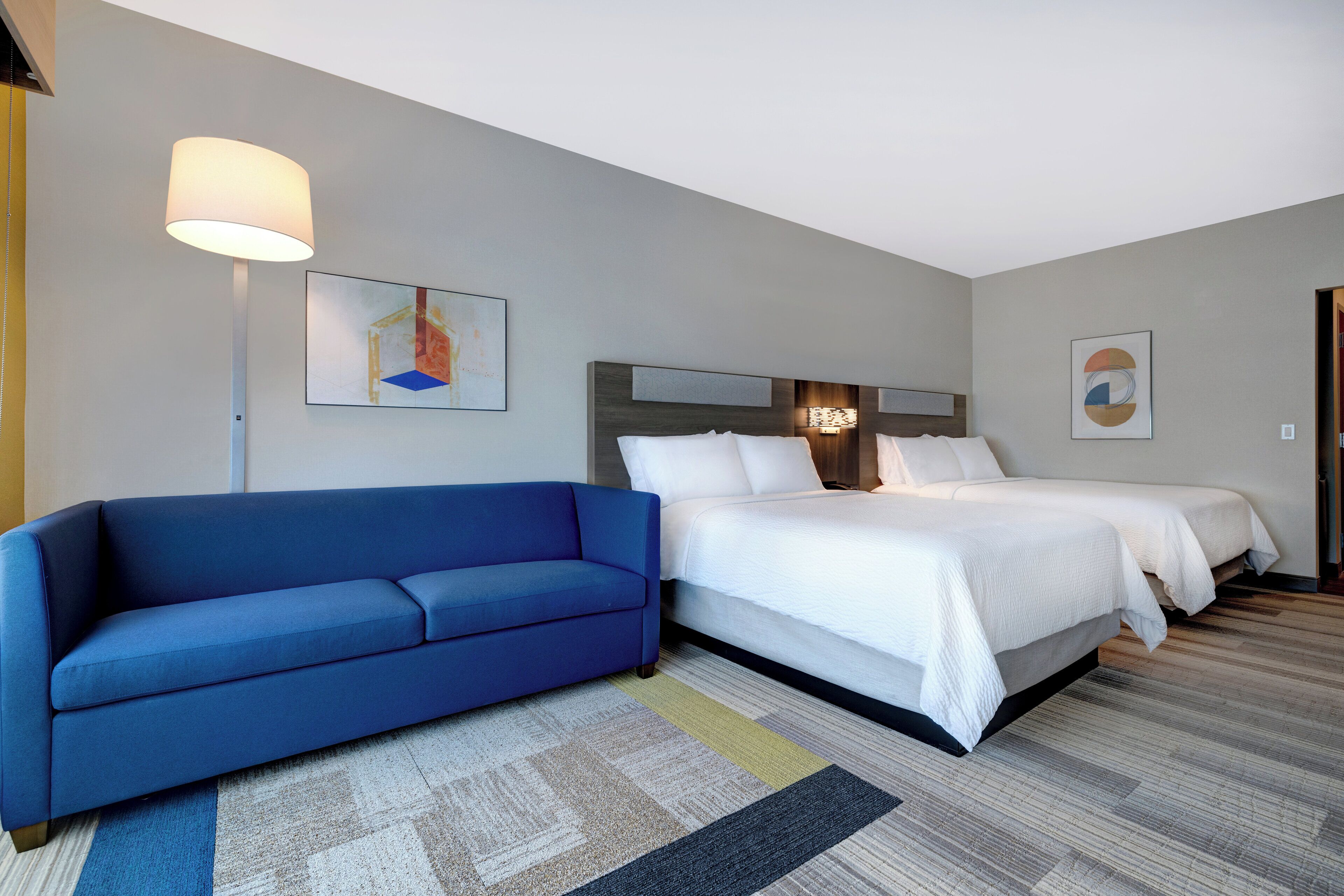 A hotel room with a blue sofa, a double bed, and two wall-mounted lamps.