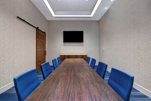 A conference room with a long wooden table, blue chairs, a mounted flat-screen TV, and a ceiling light fixture. - Holiday Inn Express & Suites Glendale Downtown by IHG (Glendale)
