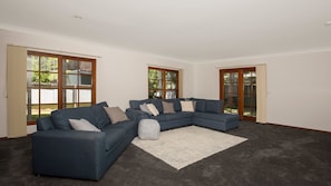 Ein Wohnzimmer mit Ecksofa, Teppich und großen Fenstern mit Holzrahmen.