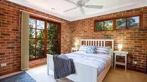 Un dormitorio con pared de ladrillo, una cama blanca, dos mesitas de noche con lámparas y un ventilador de techo.