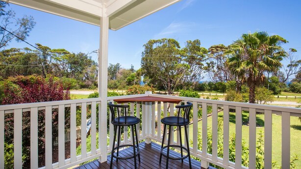 A covered outdoor area with a wooden deck, two black bar stools, and a table.