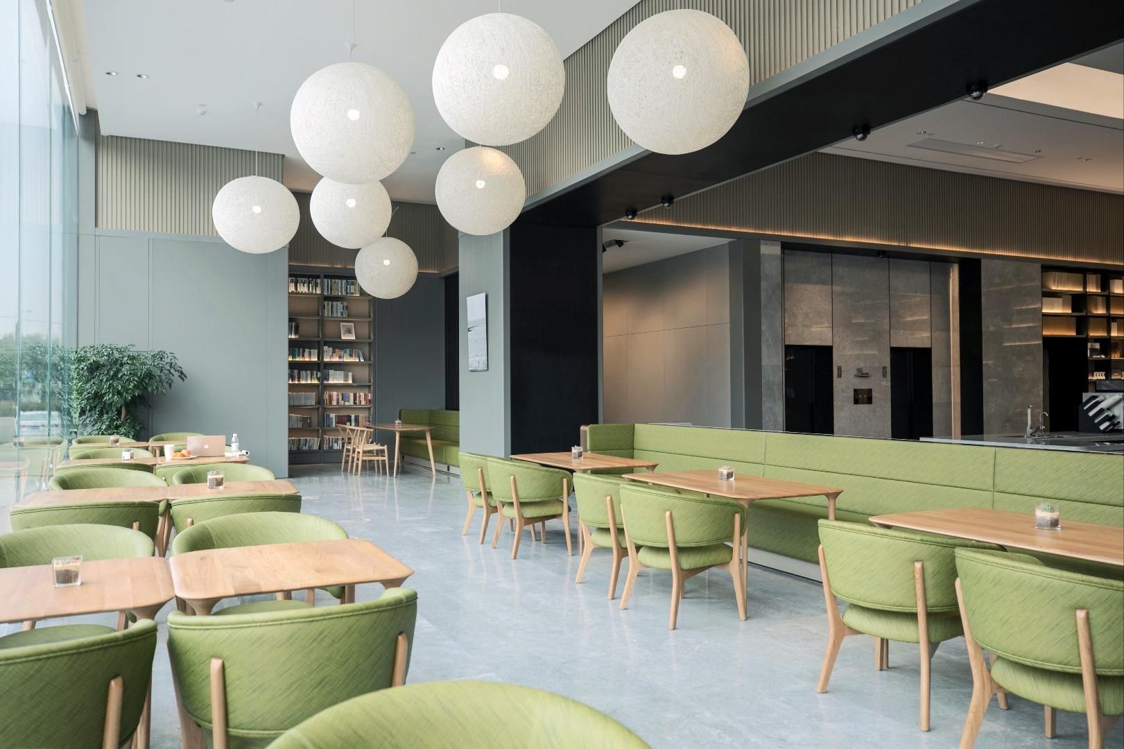 A modern library with green seating, wooden tables, and large spherical pendant lights.