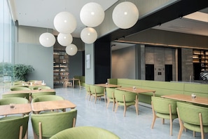Une bibliothèque moderne dotée de sièges verts, de tables en bois et de grandes suspensions sphériques.