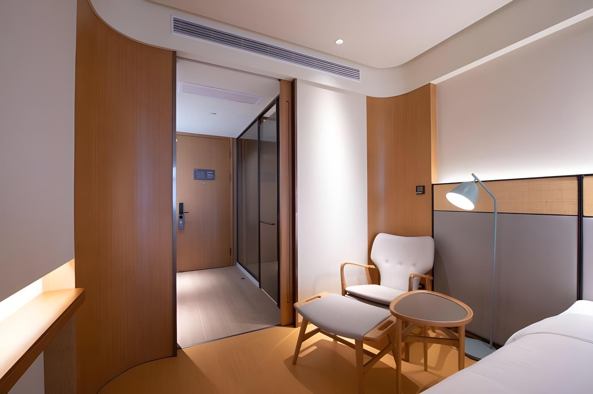 Une chambre d’hôtel moderne avec un mur d’accent en bois, une chaise blanche, une petite table ronde et une lampe de chevet.