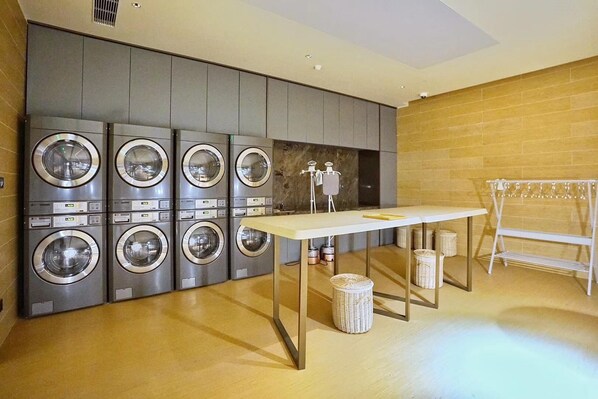 A laundry room with multiple washing machines, a table, and a bench. - Ji Hotel (Shanghai)