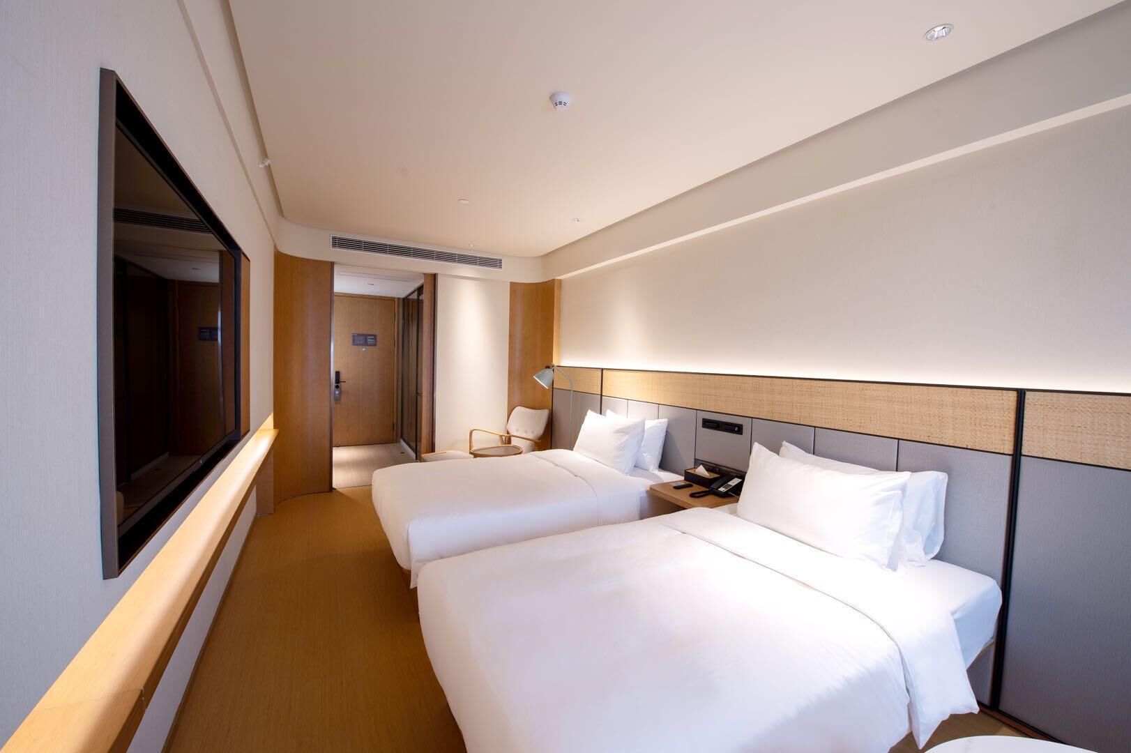 A hotel room with two beds, a TV, a desk with a lamp, and a door leading to another room.