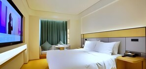 Une chambre d’hôtel avec un grand lit, une table de chevet, un téléviseur fixé au mur et une fenêtre avec des rideaux.