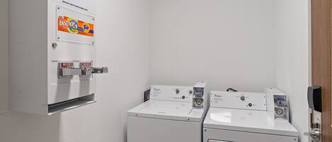 A laundry area with two washing machines, a dryer, and a wall-mounted laundry softener dispenser.