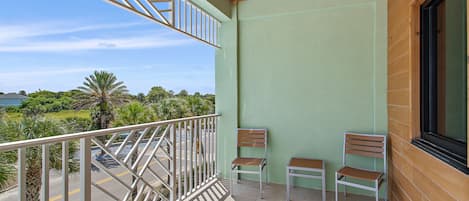 Ein Balkon mit zwei Holzstühlen, einem Metallgeländer und Blick auf eine Straße und Grünflächen.
