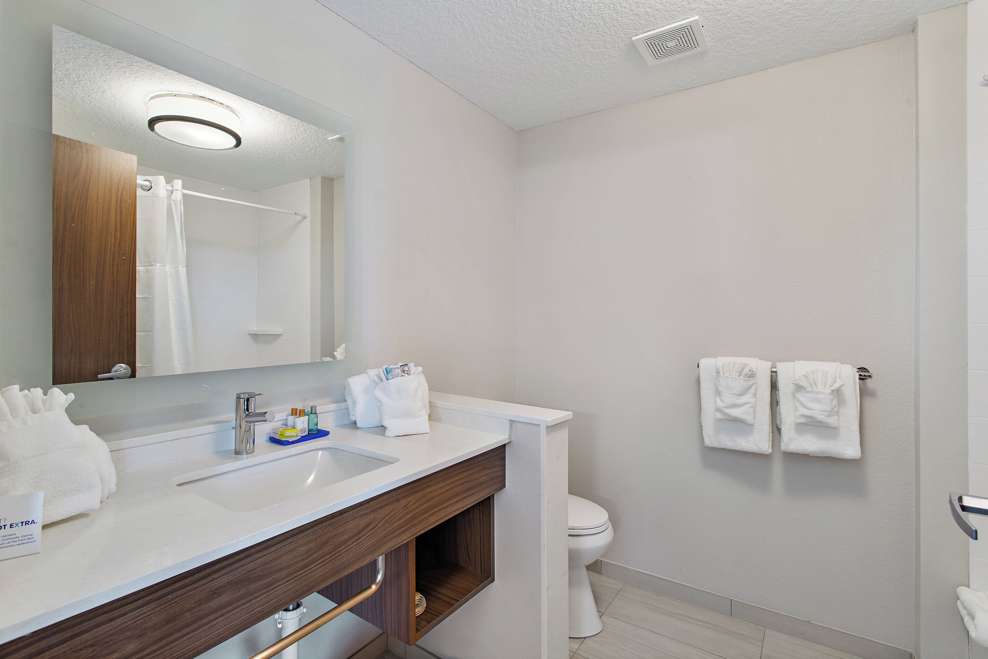 A modern bathroom with a white sink, mirror, and toilet. There are two white towels hanging on the wall.