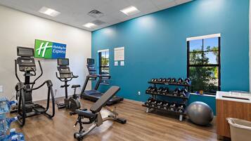 A fitness center with treadmills, elliptical machines, a bench, dumbbells, and a large exercise ball.