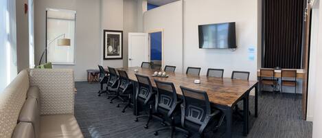 A conference room with a long table, chairs, a sofa, a TV, and a door.