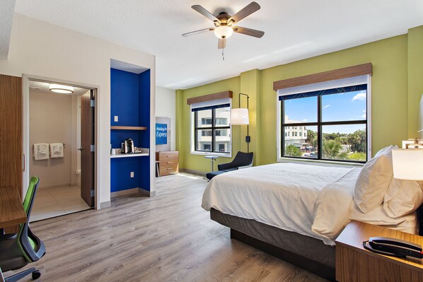 A hotel room with a bed, a desk, a chair, a window with a view, and a ceiling fan. - Holiday Inn Express St. Augustine - Vilano Beach by IHG (St. Augustine)