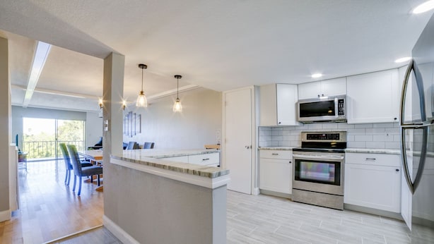 A modern kitchen with white cabinetry, stainless steel appliances, and pendant lighting.
