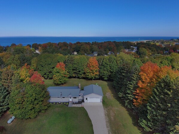 A large house with a garage, surrounded by dense trees with autumn foliage, and a view of the ocean. - Sadie Shores (Grand Marais)