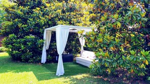 Un jardin agrémenté d’un belvédère blanc, d’une végétation luxuriante et d’un petit espace aménagé pour s’asseoir.